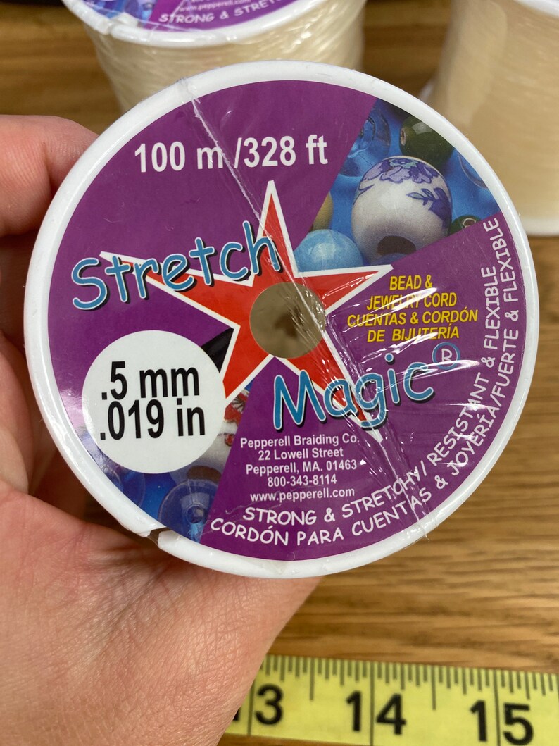 Puede incluir: Un carrete de cord&oacute;n el&aacute;stico "Stretch Magic" para cuentas y joyer&iacute;a. La etiqueta es morada y blanca, con el texto "100 m / 328 ft" y ".5 mm". El cord&oacute;n es fuerte, el&aacute;stico y flexible.