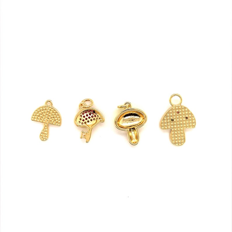 May include: Four gold-colored mushroom charms with varying designs. One charm has a textured cap and stem, while another features red accents. The charms are likely for jewelry making or crafting.