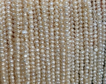 May include: A close-up of a strand of white freshwater pearls. The pearls are small and round, and they are strung together on a thin thread. The pearls are arranged in a vertical pattern, and they are all the same size.