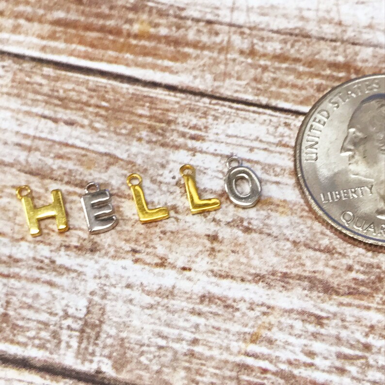 May include: Gold and silver letter charms spelling out the word "HELLO" with a US quarter for size reference.