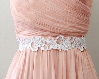 Könnte beinhalten: Ein blushfarbenes Chiffonkleid mit einem weißen Spitzenband. Das Band hat ein florales Design mit Perlenakzenten.
