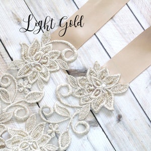 May include: Light gold floral lace applique with pearl accents and a satin ribbon. The text "Light Gold" is written in cursive. The lace is intricately designed with floral and leaf patterns, perfect for embellishments.