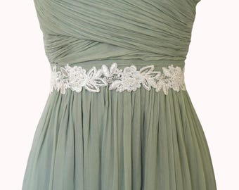 Könnte beinhalten: Salbeigrünes formelles Kleid mit einem weißen floralen Spitzenband. Das Kleid hat ein plissiertes Oberteil und einen fließenden Rock. Der Gürtel ist mit zarten, gestickten Blumen und Blättern verziert und verleiht dem Kleid Eleganz.
