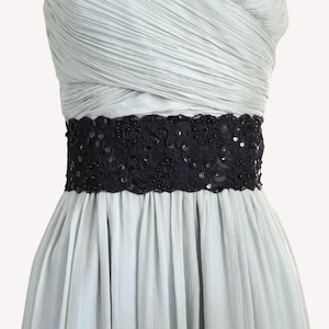 May include: A pale mint green dress featuring a strapless bodice with horizontal pleats and a wide black waistband. The waistband is decorated with intricate black lace embroidery, small black beads, and shimmering sequins throughout the fabric.