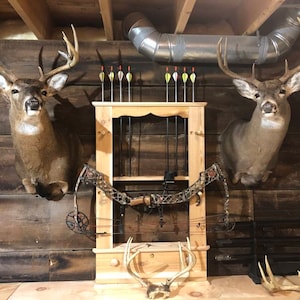 May include: A wooden wall with two mounted whitetail deer heads, a wooden bow rack with arrows, and a compound bow.