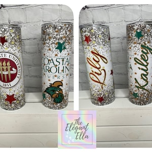 May include: Glitter-covered tumblers with university logos and names. One tumbler features the Coastal Carolina University logo and another has the name "Lily" in red. The tumblers are decorated with gold stars and red and green accents.
