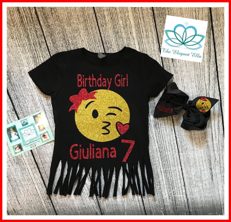 May include: Black t-shirt with a gold glitter winking emoji with a red bow and red heart. The text "Birthday Girl" and "Giuliana 7" are in red glitter. The shirt has a frayed bottom.