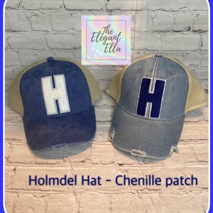 May include: Two blue denim trucker hats with a beige mesh back. One hat has a white chenille letter "H" and the other has a blue chenille letter "H". The hats are on a brick wall background.  Holmdel Hat - Chenille patch.