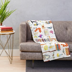 May include: White throw blanket with a watercolor pattern of various magical objects, including books, wands, owls, potions, and a scarf. The pattern is repeated throughout the blanket.