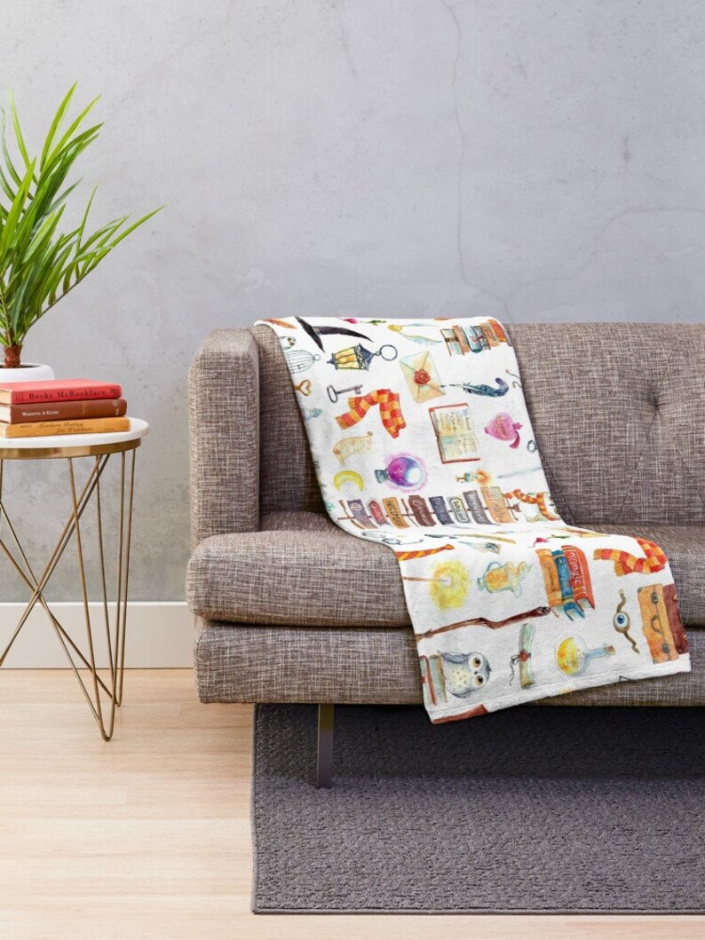 May include: White throw blanket with a watercolor pattern of various magical objects, including books, wands, owls, potions, and a scarf. The pattern is repeated throughout the blanket.