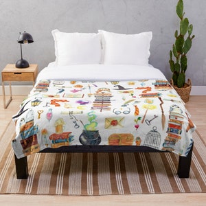 May include: A white throw blanket with a watercolor pattern of various magical objects, including books, owls, wands, potions, and a cauldron. The pattern is on a white background and is surrounded by a white border.