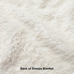 May include: Close-up of the soft, white, fluffy back side of a sherpa blanket. The texture is visible and the blanket appears very cozy.