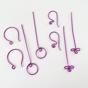 May include: A selection of purple wire earring components, including hooks, straight wires, and decorative elements. The components are arranged on a white surface, showcasing their various shapes and designs. These are ideal for DIY jewellery making.
