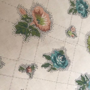 May include: A white fabric with a quilted pattern and a floral print. The flowers are in shades of pink, blue, and green.