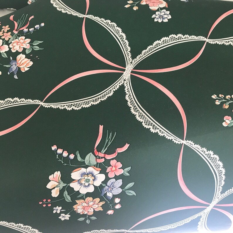 Puede incluir: Una tela verde con un patr&oacute;n de encaje blanco y lazos de cinta rosa. La tela presenta un dise&ntilde;o floral con flores rosas, blancas y verdes.
