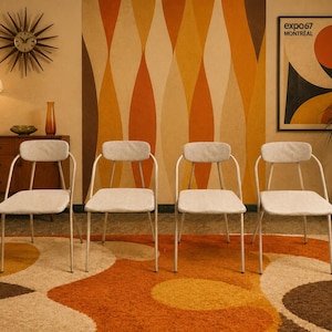 May include: A set of four chairs with off-white upholstered seats and backrests, supported by thin, light-colored metal frames. Each chair features a curved backrest and four slender legs, providing a uniform appearance across the group.