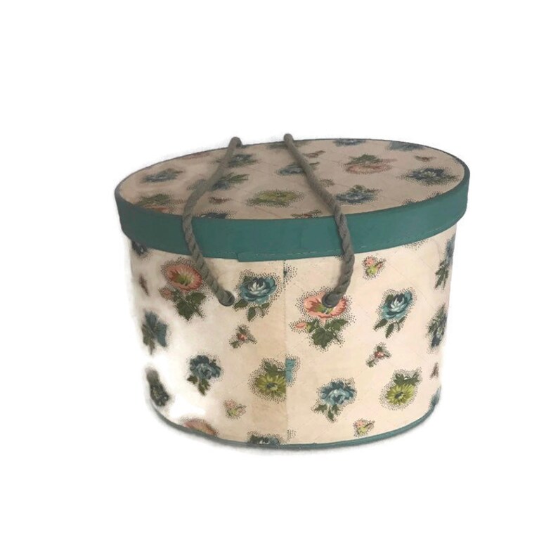 May include: A vintage hat box with a floral pattern and a teal trim. The box has two rope handles.