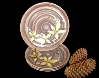 May include: Set of four brown ceramic plates with a swirling pattern and yellow floral design. The plates are stacked on a metal stand.
