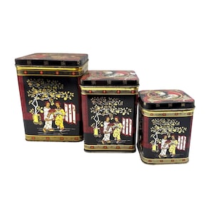 May include: Set of three black metal storage tins with lids. Each tin features a decorative Asian-inspired design with figures, trees, and red accents. The tins are of varying sizes, perfect for kitchen or home decor.
