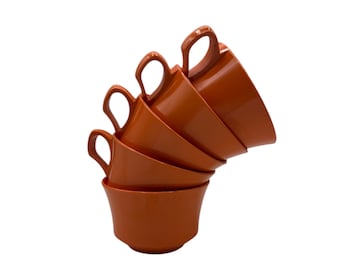May include: A stack of five orange ceramic mugs with handles. The mugs are nested together and are angled to the right.