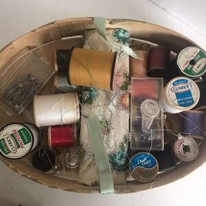 May include: A wooden sewing box filled with various sewing supplies, including spools of thread in different colors, needles, pins, and a thimble. The box also contains a small piece of fabric with a floral pattern.