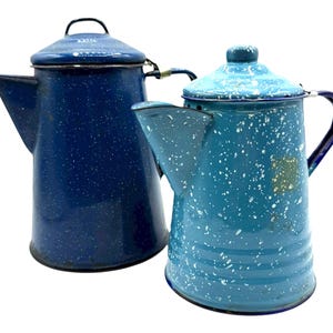 May include: Two vintage enamelware coffee pots. One is a dark blue with white speckles, the other is a lighter blue with white speckles. Both have lids, spouts, and handles. The coffee pots are likely from the mid-20th century.