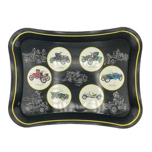 May include: A black metal tray with a yellow rim features eight vintage cars in circular white frames. Each car is labeled with its name and year of manufacture.