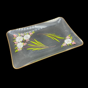 May include: A clear glass serving tray with a gold rim and a floral design. The flowers are pink and white with green leaves.