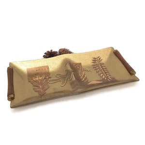 May include: A gold-toned glass serving tray with a wood-like design and wooden handles. The tray features a stylised design of leaves and branches.