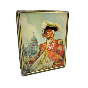 May include: Vintage tin box with a gold trim and a colorful image of a man in a red and gold uniform with a white hat and a building in the background.