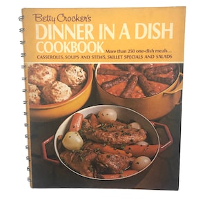 May include: A vintage cookbook titled "Betty Crocker's Dinner in a Dish Cookbook" with a yellow cover and a spiral binding. The cover features three photos of different dishes: a casserole with dumplings, a skillet dish with sausages, and a stew with meat and vegetables.