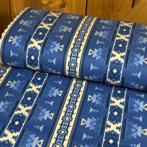 May include: A roll of blue fabric with a geometric pattern. The design features vertical stripes with alternating cream and blue shapes, including diamonds, triangles, and stepped lines. The fabric is suitable for various crafting projects.