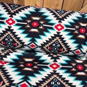 May include: A rolled-up blanket with a Southwestern geometric pattern. The design features black, white, turquoise, red, and brown shapes. The blanket has a white border.