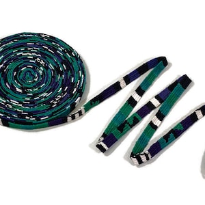 May include: A roll of green, blue and white patterned ribbon with a black stripe. The ribbon is woven and has a geometric design.