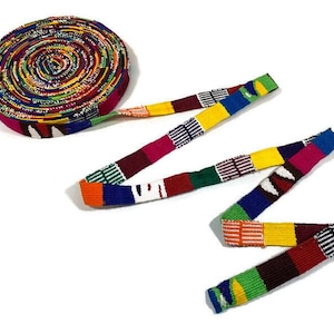 May include: A colourful woven ribbon with a variety of colours including red, yellow, green, blue, and white. The ribbon is rolled up and tied in a knot.