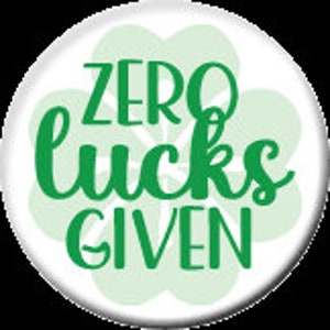 May include: A white button with a green four-leaf clover design. The text "ZERO LUCKS GIVEN" is written in green cursive lettering.