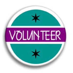 May include: Teal round button with a white stripe and the word "VOLUNTEER" in white letters. Two black stars are on either side of the stripe.