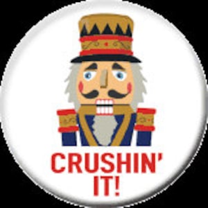 May include: A round button featuring a cartoon nutcracker in a blue and gold uniform with a tall hat. The text "CRUSHIN' IT!" is in red below the nutcracker.