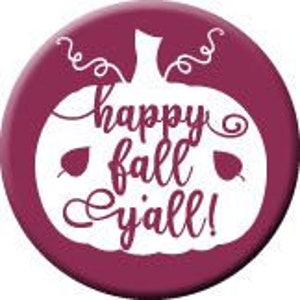 Può includere: Un bottone bordeaux con un design a zucca bianca e la scritta "happy fall y'all!". La zucca ha un gambo e due foglie. Il bottone è rotondo e probabilmente usato come spilla o distintivo decorativo.