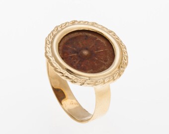 May include: A gold ring with a round bezel featuring a brown coin with a raised center. The bezel is decorated with a rope-like design.
