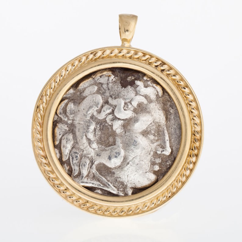 May include: A gold pendant with a rope-like border, featuring a silver coin with a profile of a person's head.