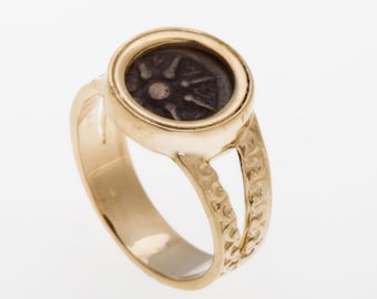 May include: A gold ring with a circular design. The ring features a dark brown coin with a star-shaped design in the center. The coin is set in a gold bezel.