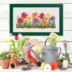 Puede incluir: Un bordado de punto de cruz enmarcado que representa un jardín de flores colorido con una valla de madera y un pequeño ratón asomándose desde detrás de las flores. Las flores son rojas, amarillas, moradas y naranjas.