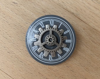 Okrągła broszka w stylu steampunk z przekładnią: szara tarcza zegarka z metalowymi przekładniami