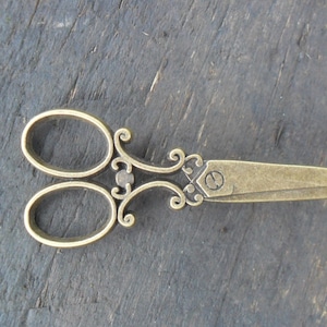 May include: A pair of ornate gold-toned scissors with a decorative design on the handles. The scissors have a small letter "E" engraved on the blade.