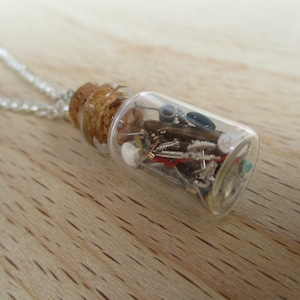 May include: A silver chain necklace with a small glass bottle pendant filled with various metal gears, screws, and other small objects.