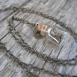May include: A brass chain necklace with a small glass bottle pendant filled with tiny gears and a cork stopper.