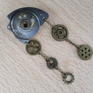 Peut inclure: Un bijou de style steampunk composé d'un engrenage argenté avec une chaîne attachée à quatre petits engrenages en laiton. La chaîne est reliée à un plus grand engrenage en laiton avec un motif décoratif.