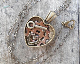 Collar con medallón de corazón, llave de bronce y engranaje de cobre, en una cadena de corazones entrelazados de 53 cm.