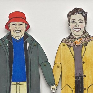 May include: Two paper dolls, one wearing a red hat and a green jacket, the other wearing a yellow jacket with a patterned scarf.